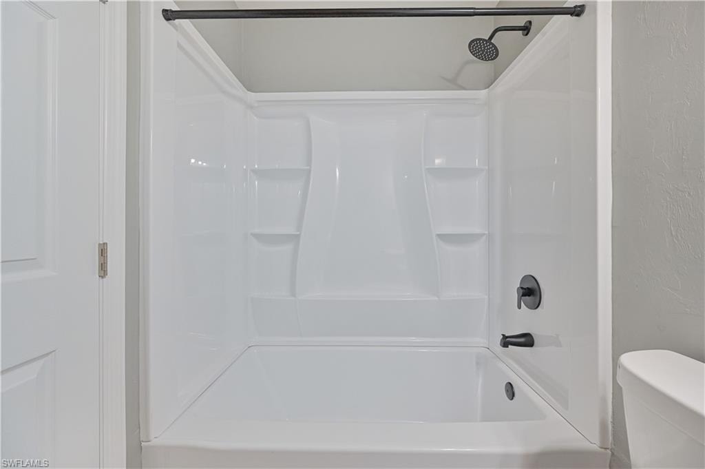 White bathtub and shower combination unit featuring integrated shelving, a matte black showerhead, and coordinating matte black tub filler and control