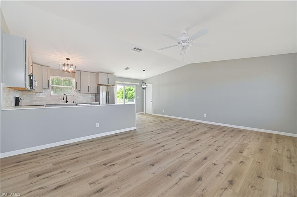 Spacious open-concept living area featuring wood-finish flooring, vaulted ceilings, and a contemporary ceiling fan
