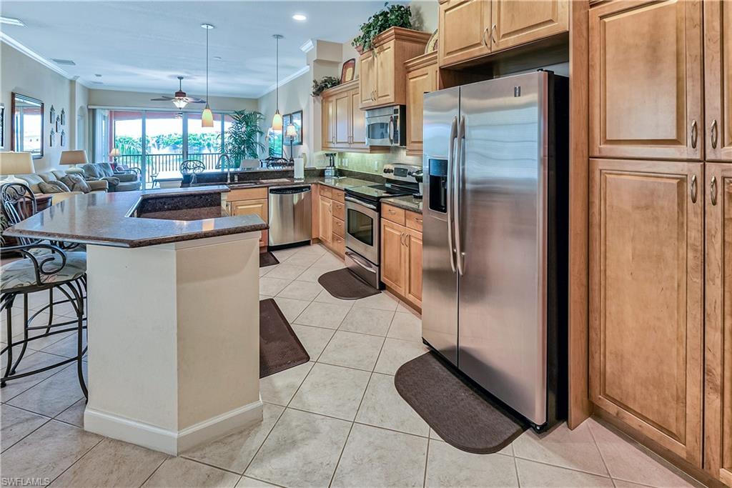 Kitchen with appliances with stainless steel finishes, open floor plan, dark stone counters, ornamental molding, and a kitchen bar