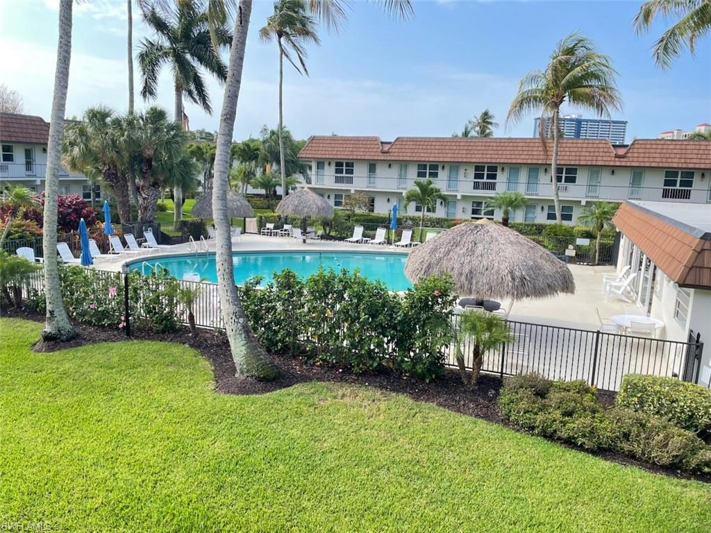Community swimming pool with surrounding concrete deck, two thatched roof cabanas, and mature palm trees