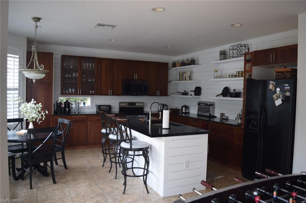Gourmet kitchen with rich wood-finish cabinetry, black countertops, and a white shiplap accent wall