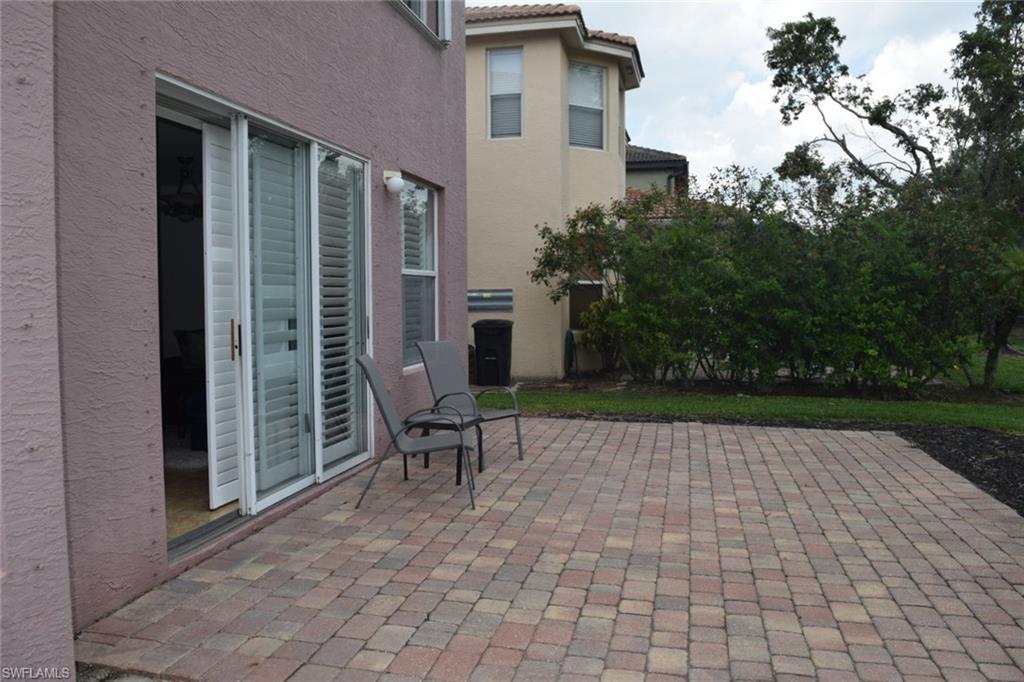 Paved patio featuring multi-toned pavers, direct access via sliding glass doors with interior shutters, and a surrounding privacy hedge