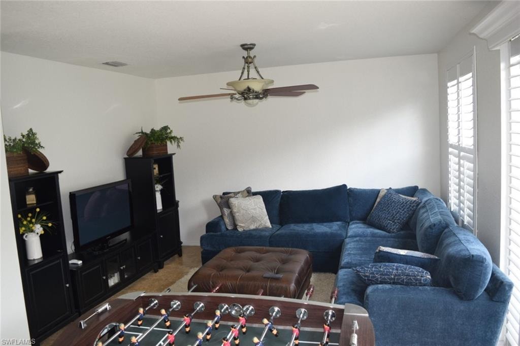 Living area featuring white walls, wood-finish flooring, and a ceiling fan with integrated lighting