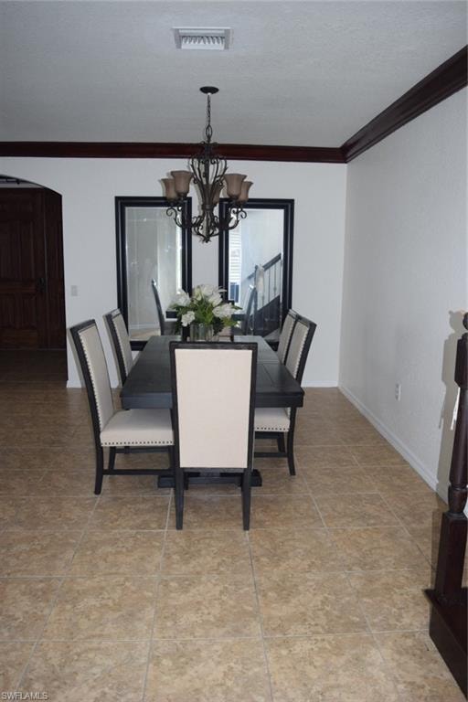 Formal dining area featuring a bronze chandelier with amber glass shades, decorative ceiling trim, and large format tile flooring