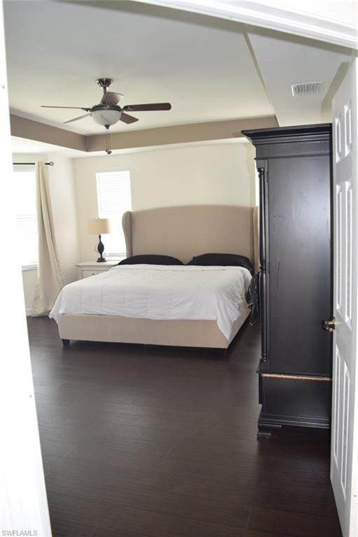 Room featuring dark wood-finish flooring, a tray ceiling with a ceiling fan, and light-colored walls