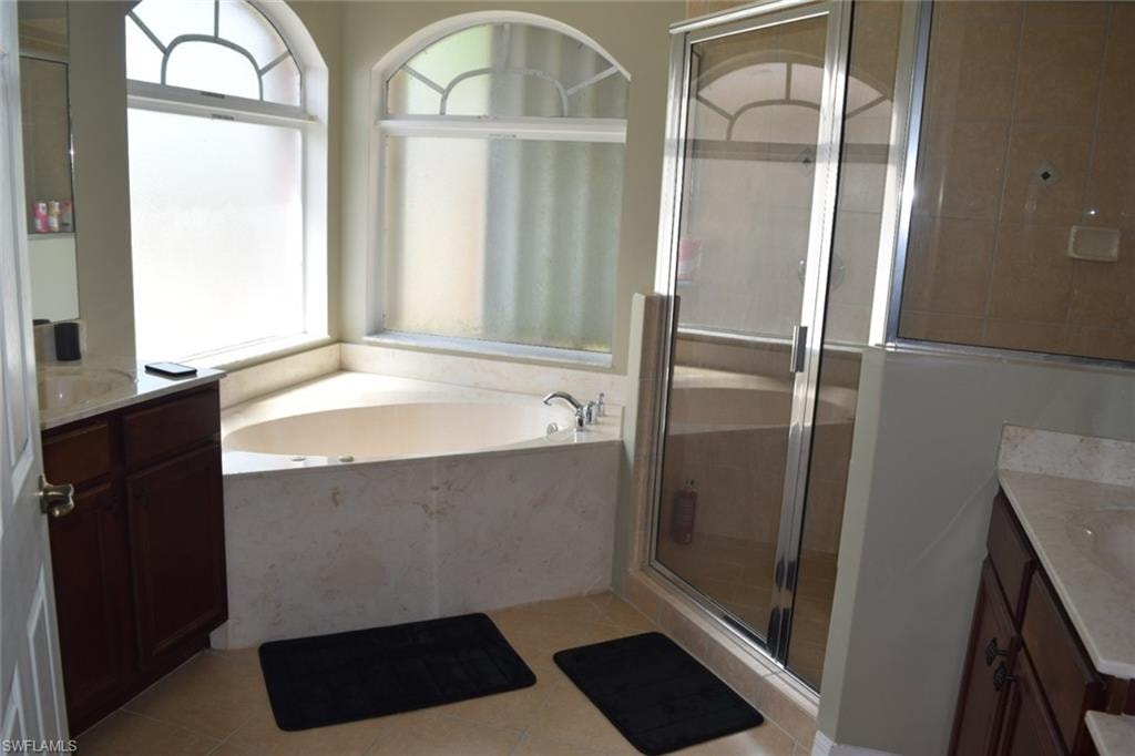 Bathroom featuring a built-in corner soaking tub with arched windows, a glass-enclosed shower, dual vanity areas with undermount sinks, and tile flooring