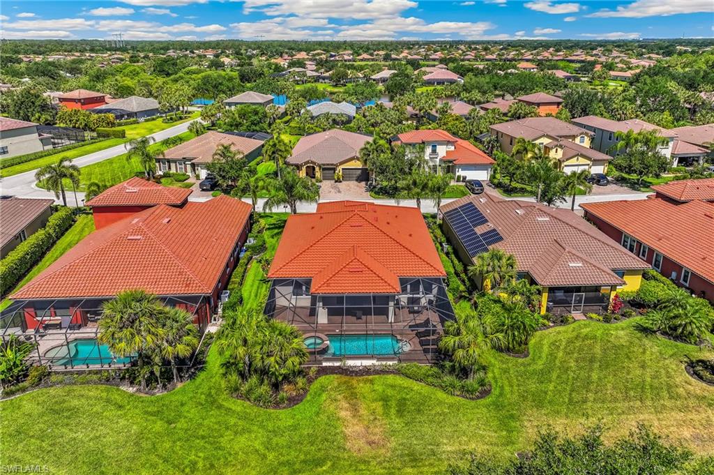 Residential property featuring a terracotta tile roof, screened lanai, inground pool, and surrounding mature landscaping