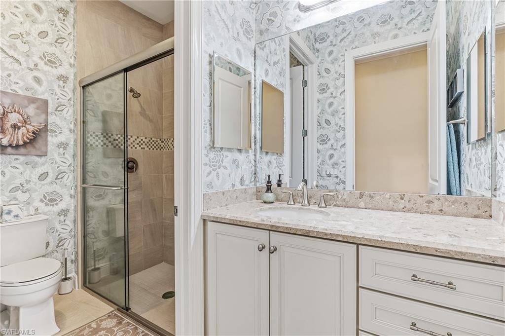 Bathroom featuring a built-in vanity with light-toned cabinetry and a light-toned countertop, an undermount sink with a chrome faucet, a large wall-mounted mirror, and a glass-enclosed shower with tiled walls and a decorative mosaic band