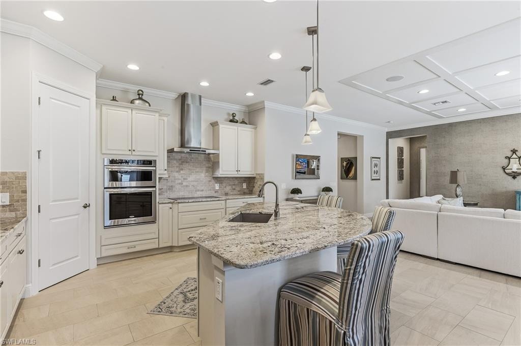 Modern kitchen featuring a curved island with stone countertop, pendant lighting, built-in stainless steel appliances, white cabinetry, and a tile backsplash