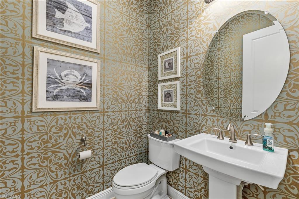 Pedestal sink with brushed nickel faucet, oval mirror, and patterned wallpaper