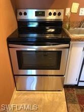 Detailed view of stainless steel range with electric stovetop, baseboards, and white cabinetry