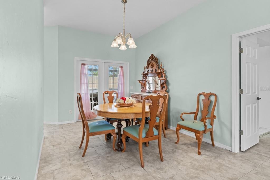 Vaulted ceiling with a brass-finish chandelier, ceramic tile flooring, and french doors with exterior access