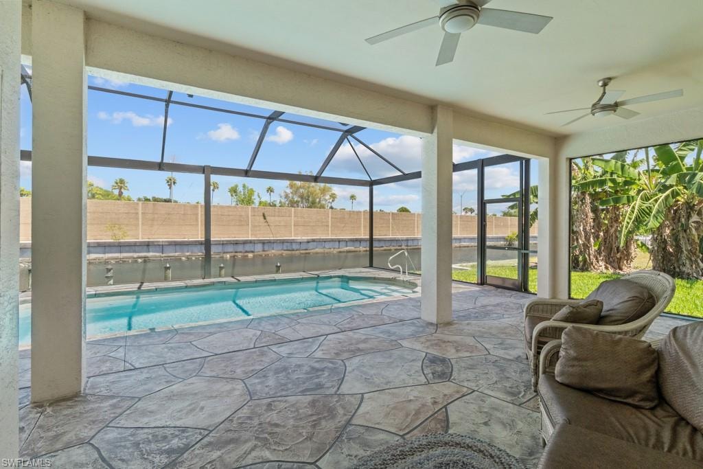 Expansive screened lanai featuring a swimming pool, patterned stone-look flooring, and dual ceiling fans