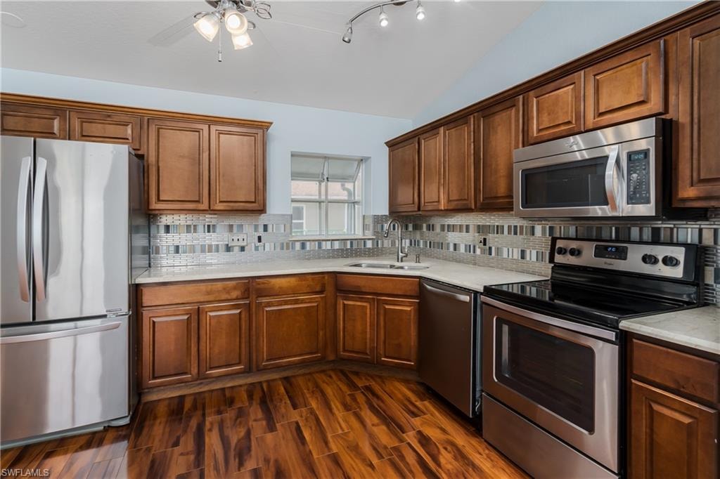 Kitchen featuring stainless steel appliances, wood-finish flooring, wood cabinetry, light-toned countertops, and a tiled backsplash