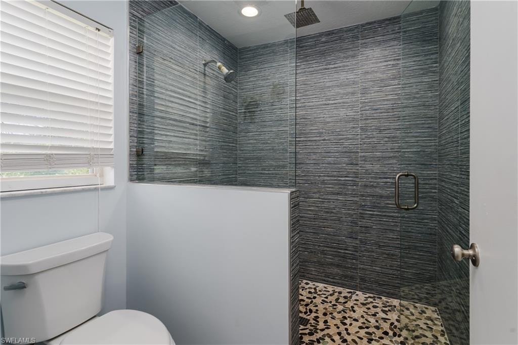 Walk-in shower featuring glass enclosure, textured dark tile surround, rainfall showerhead, and pebble flooring