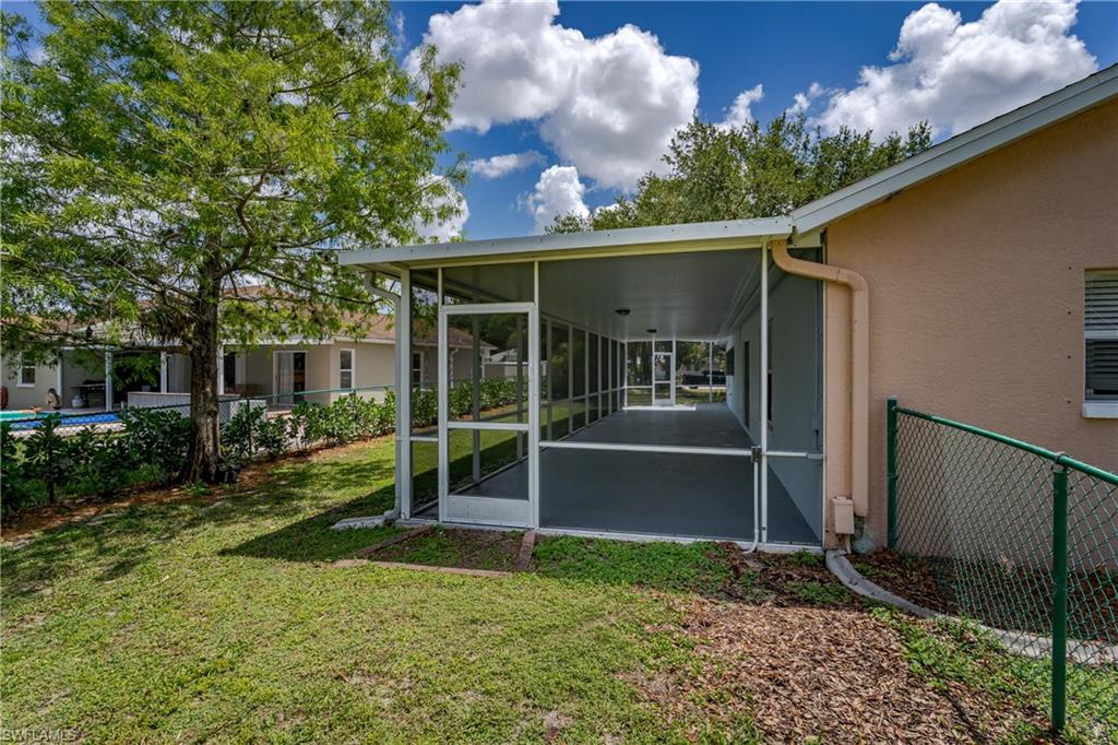Expansive screened patio featuring a concrete floor, white frame, and a door leading to a spacious backyard with a manicured lawn and mature tree