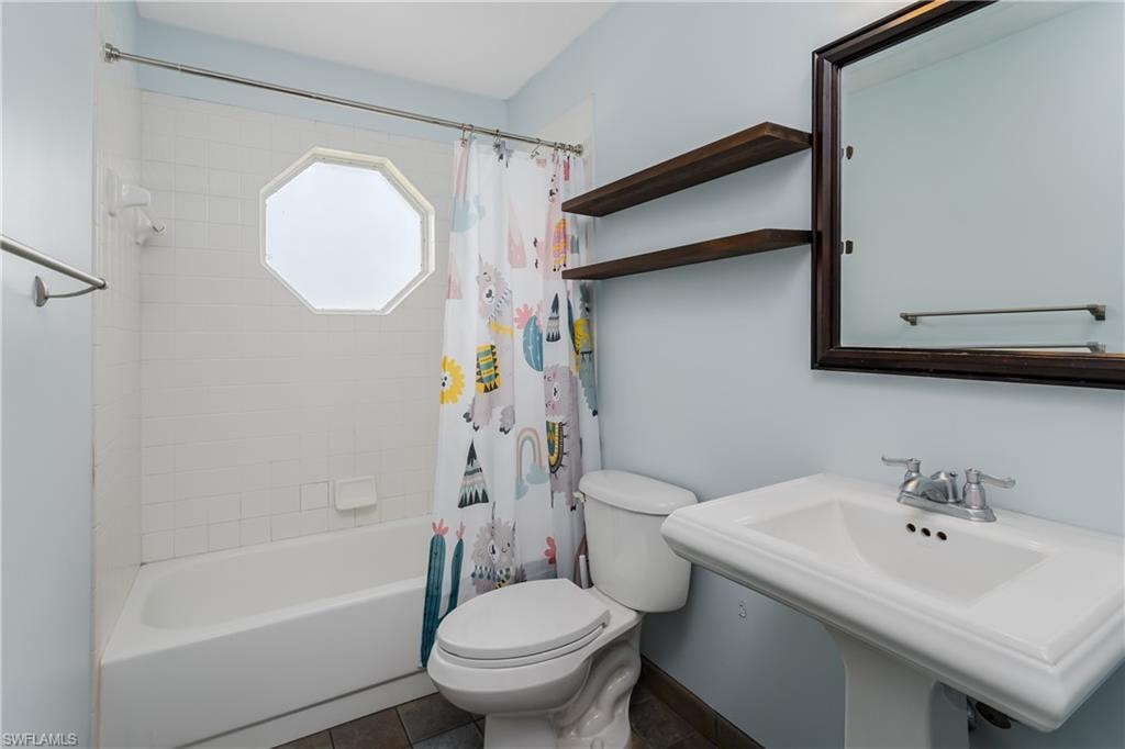 Bathroom featuring a pedestal sink, framed mirror, and wood-finish shelving