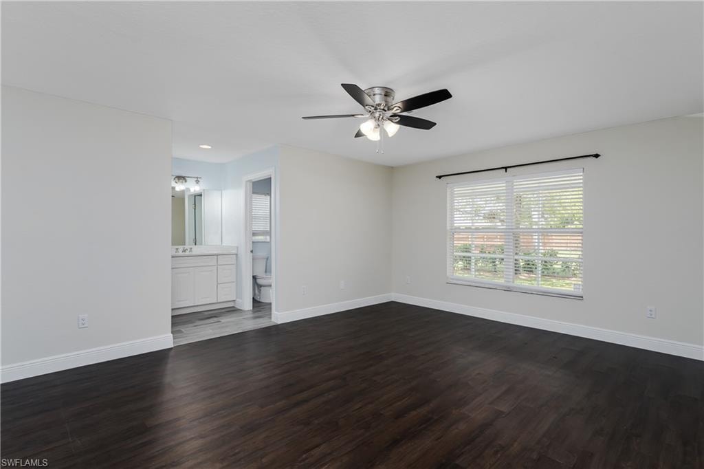 Spacious room featuring dark wood-finish flooring, a ceiling fan with integrated lighting, and a large window with white blinds