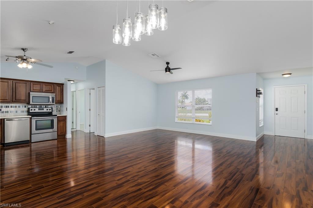 Open-concept living area featuring rich wood-finish flooring, vaulted ceilings, and a modern chandelier