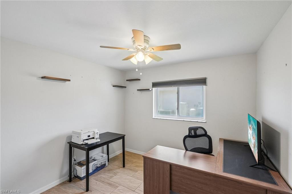 Room featuring neutral-toned tile flooring, a window with a roller shade, and a ceiling fan with light fixture
