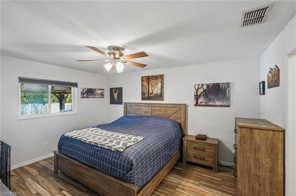 Bedroom featuring wood-finish flooring, a ceiling fan with integrated lighting, and a window with roller blinds