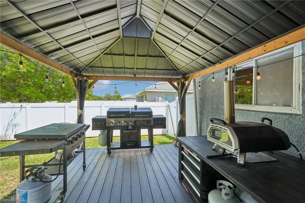 Covered patio featuring composite decking, a metal gazebo roof, string lighting, and a privacy fence