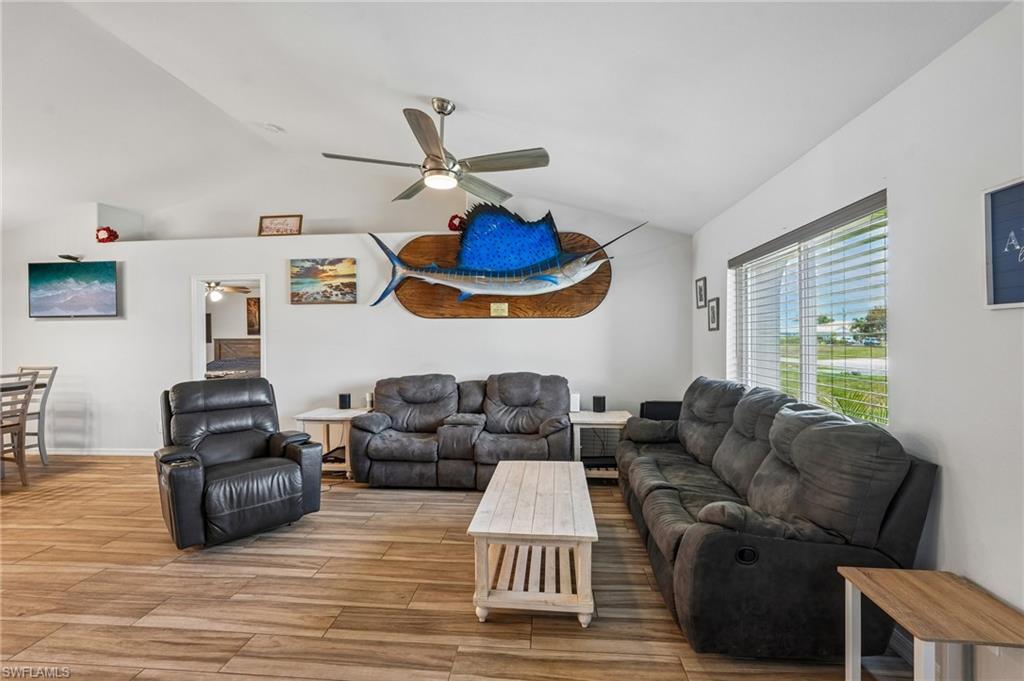 Vaulted ceilings crown this living space, featuring wood-finish flooring and a ceiling fan with integrated lighting