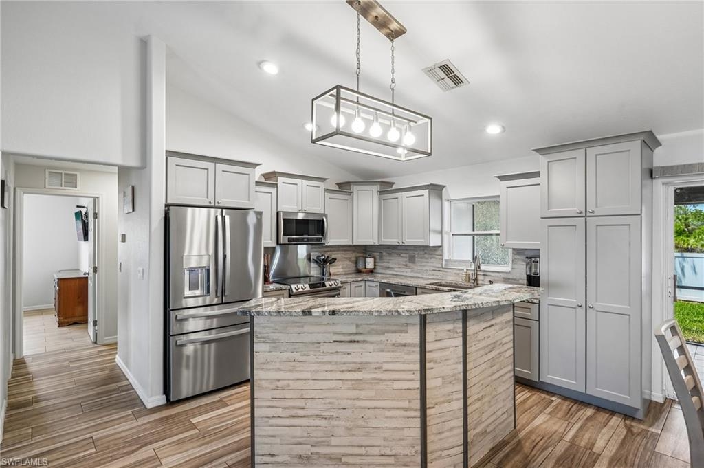 Kitchen featuring light gray shaker cabinetry, stainless steel appliances, a center island with a wood-finish facade and granite countertop, and wood-finish flooring