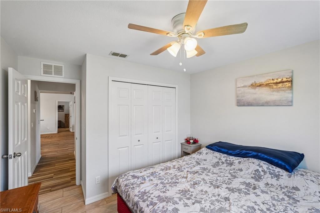 Bedroom featuring light gray walls, wood-finish flooring, a ceiling fan with light fixture, and bifold closet doors