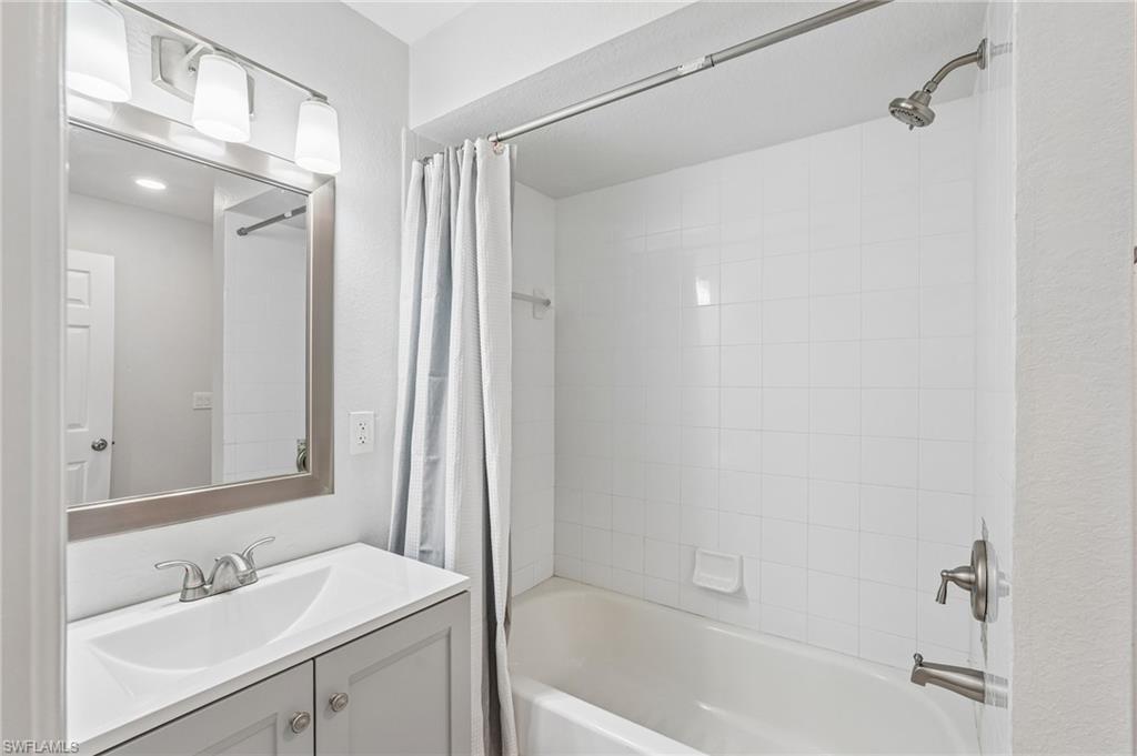 Bathroom featuring a white bathtub with subway tile surround, brushed nickel fixtures, a vanity with a white countertop and integrated sink, a rectangular mirror, and a three-light vanity bar