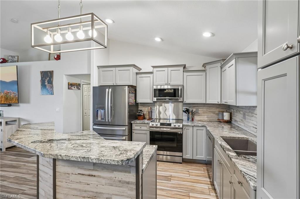 Kitchen featuring light wood-finish flooring, light gray cabinetry, stainless steel appliances, and a U-shaped island with a marbled countertop