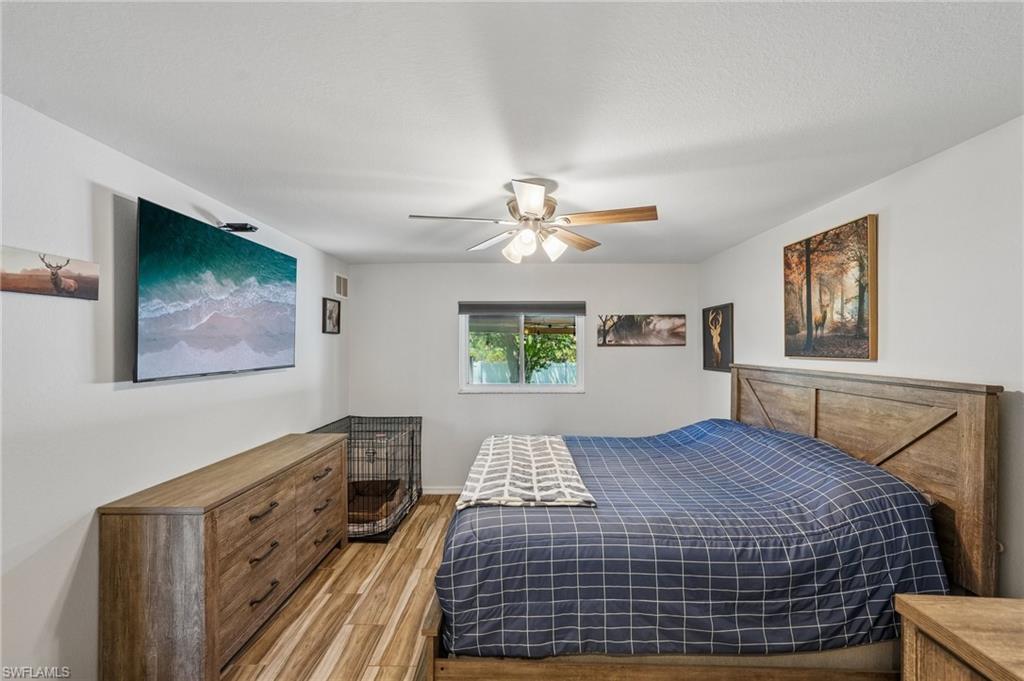 Bedroom featuring wood-finish flooring, a ceiling fan with integrated lighting, a window with roller shades, and white painted walls