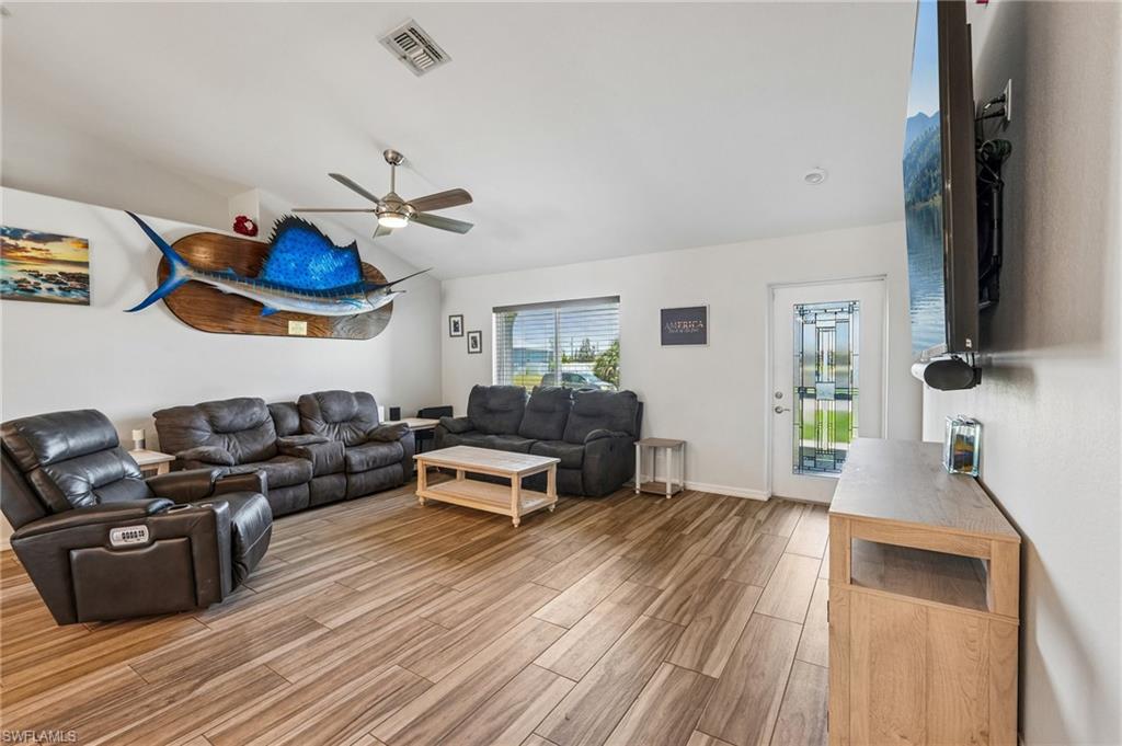 Spacious living area featuring wood-finish tile flooring, a vaulted ceiling, and a ceiling fan