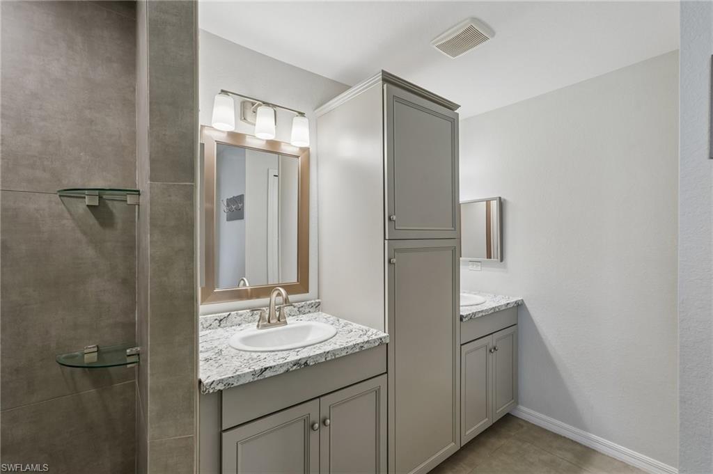 Bathroom featuring a dual vanity with light gray cabinetry and granite-finish countertops