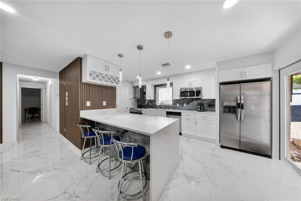 Contemporary kitchen featuring an oversized island with a solid surface countertop, white shaker cabinetry, stainless steel appliances, and large format marble-look tile flooring