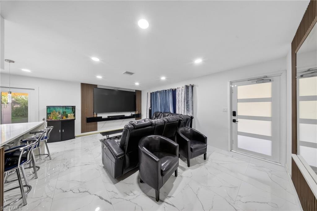 Open-concept living space with large format porcelain tile flooring, recessed lighting, and a contemporary media wall with wood-finish paneling