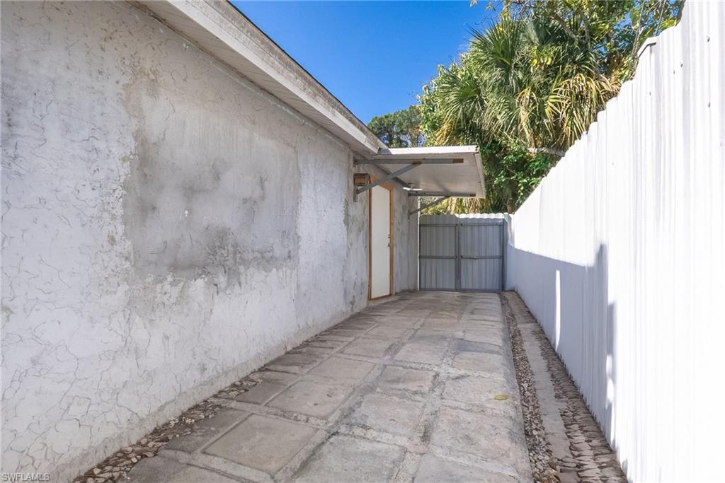 Concrete paver pathway with gravel edging, bordered by a textured stucco wall and a white corrugated fence