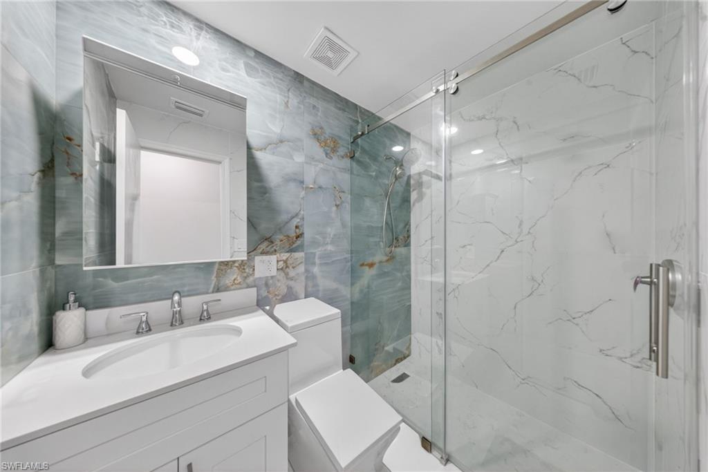 Bathroom featuring a walk-in shower with clear glass enclosure, white vanity with integrated sink, modern chrome faucet, and full-height wall tiling