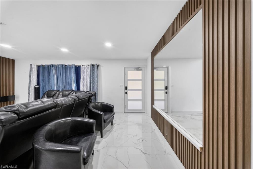 Entertainment space featuring a full-wall mirror with vertical wood-finish paneling, recessed lighting, and white marble-look tile flooring