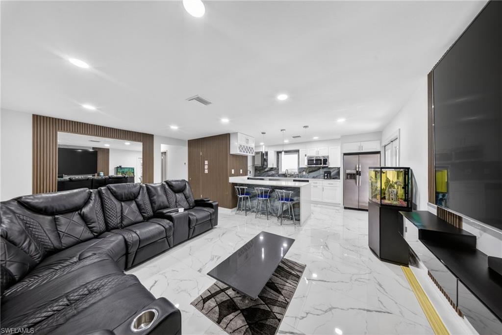 Open-concept living space featuring white marble-look flooring, recessed lighting, and a kitchen island with seating