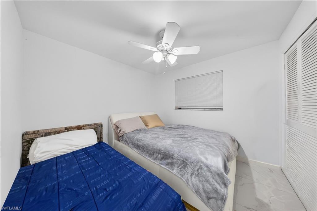 Bedroom featuring a white ceiling fan with integrated lighting, a window with horizontal blinds, and a built-in louvered closet