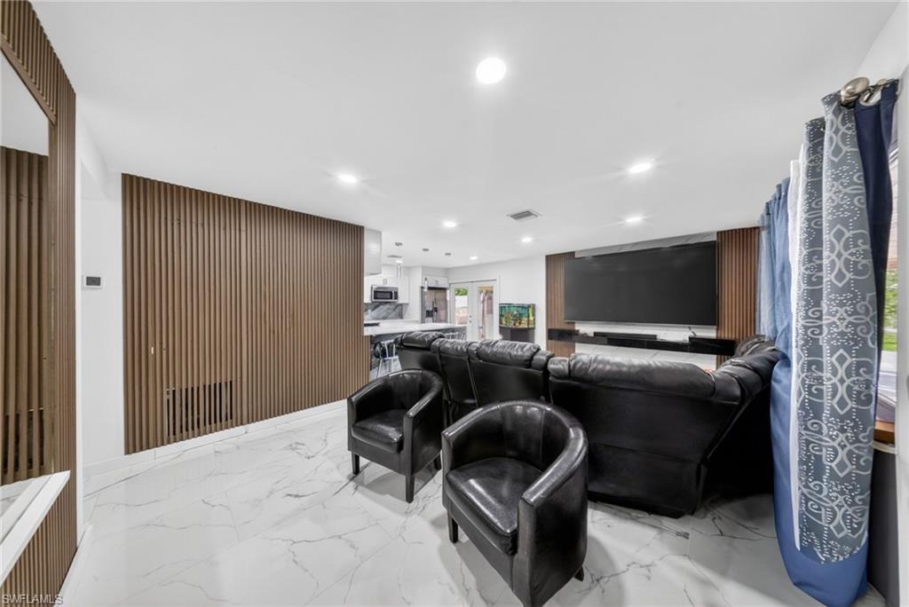 Open-concept living area featuring white marble-look tile flooring, recessed lighting, a slatted wood-finish accent wall, and a built-in media console