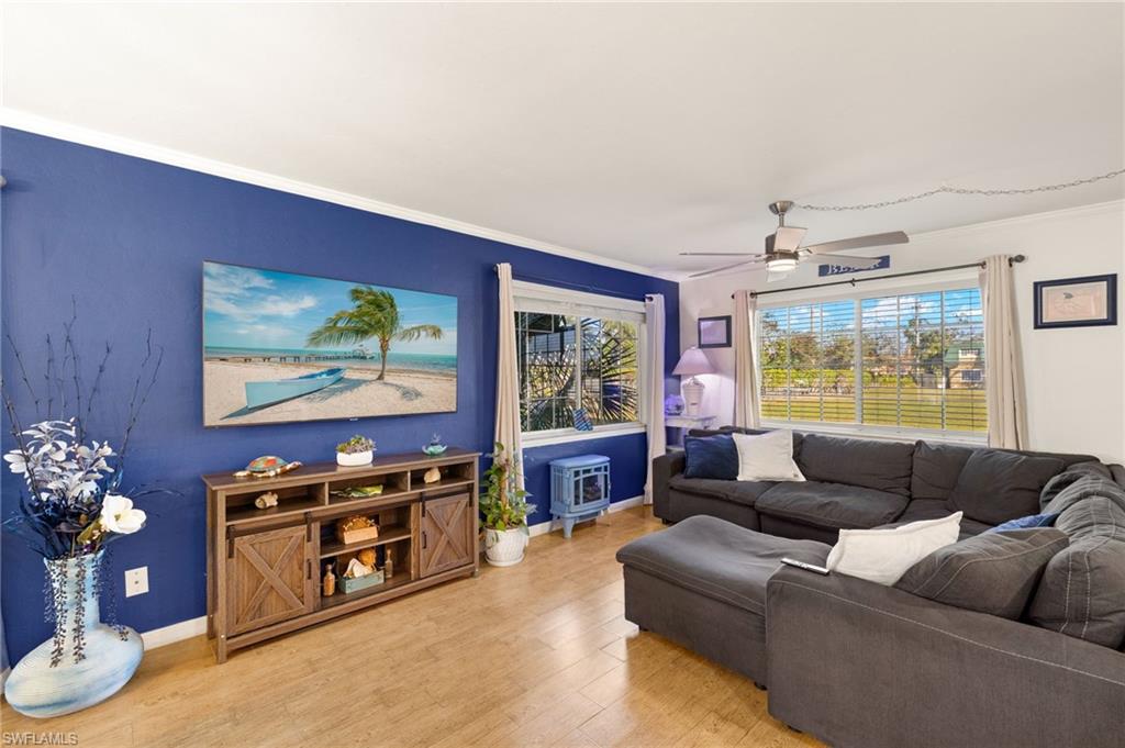 Living room with wood finished floors, a ceiling fan, and crown molding
