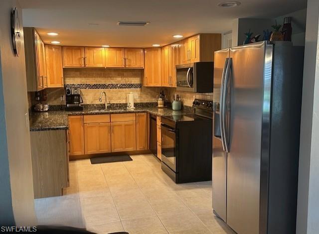 Kitchen with appliances with stainless steel finishes, backsplash, light tile patterned floors, and dark stone counters