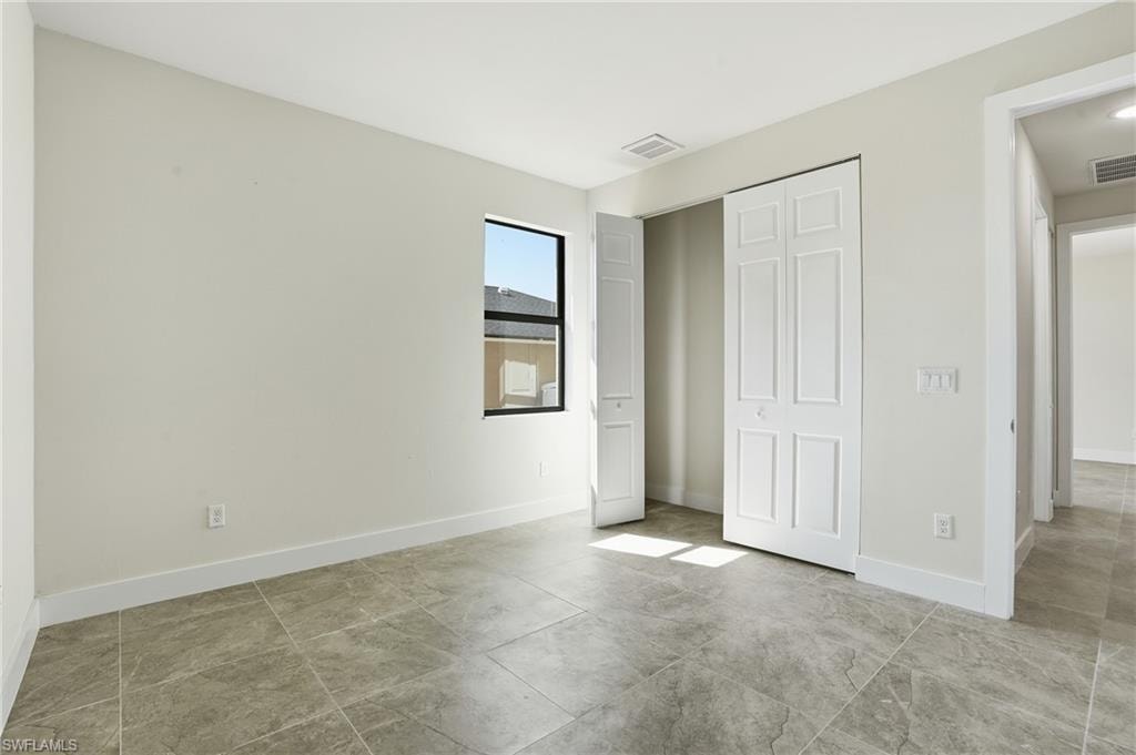 Spacious interior room featuring light-toned walls, a rectangular window with dark trim, bi-fold closet doors, and large format tile flooring