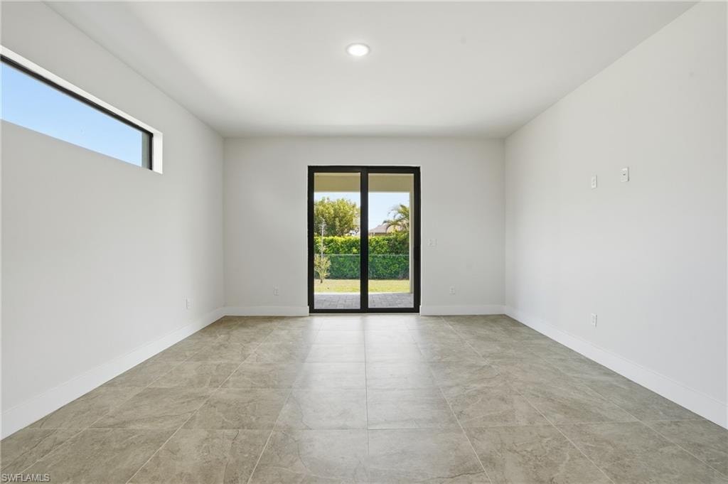 Spacious interior featuring a sliding glass door, transom window, recessed ceiling lighting, light-toned tile flooring, and white baseboards