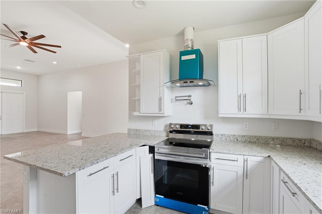 Contemporary kitchen featuring white cabinetry with silver hardware, speckled stone countertops, and a stainless steel range with a wall-mounted range hood