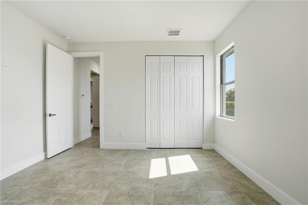 Neutral-toned bedroom featuring large format tile flooring, a white bi-fold closet, a white panel door with dark hardware, a single window, and white baseboards