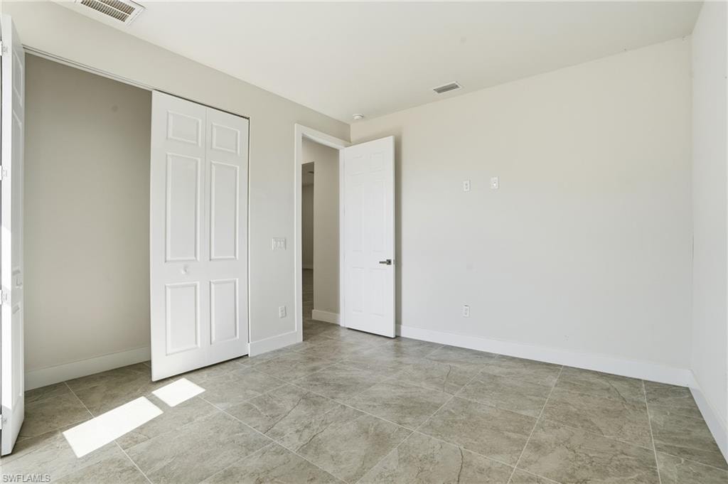 Spacious room featuring large format tile flooring, white bi-fold closet doors, white baseboards, and a white interior door