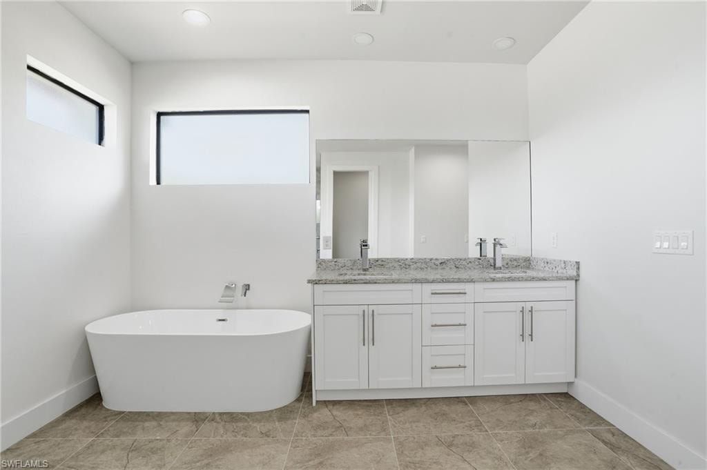 Modern bathroom featuring a freestanding tub, dual vanity with white cabinetry, polished chrome fixtures, and a granite countertop